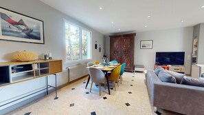A modern living room with a dining area, a large window, a TV, and a wooden cabinet.