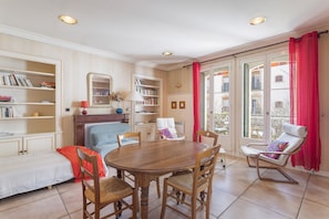 A room with a wooden dining table, chairs, a sofa, a bookshelf, a mirror, and a window with curtains.