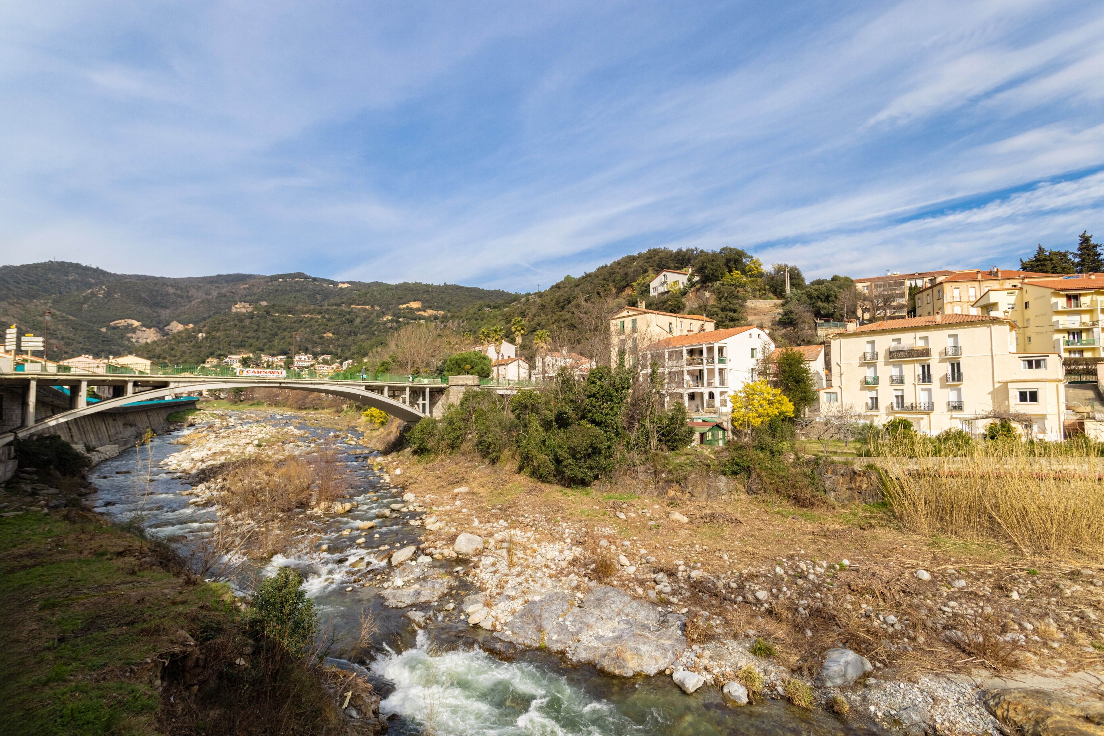 Une rivière traversée par un pont, avec des bâtiments et des collines en arrière-plan.