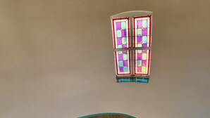Una scala a chiocciola con ringhiera in legno e dettagli blu, che conduce a una finestra con vetrate colorate.