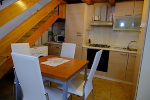 Une cuisine de taille réduite avec une table à manger en bois, des chaises blanches et un four à micro-ondes.