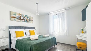 Quarto de hotel com cama, escrivaninha, cadeira, janela com cortinas e um quadro na parede.