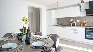 Uma cozinha moderna com armários brancos, uma área de jantar com uma mesa redonda posta para quatro pessoas e vista para o quarto adjacente.