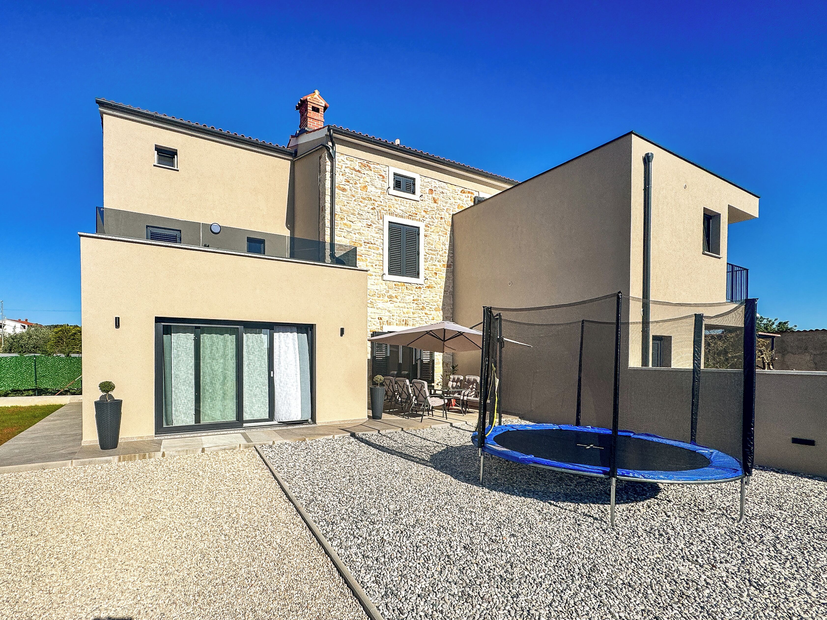 A modern house with a stone facade, a large patio with a trampoline, and a covered outdoor seating area.