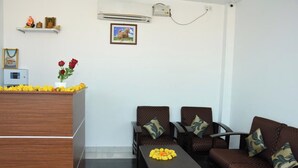 Ein Empfangsbereich mit einem Holztisch, zwei braunen Sofas mit gemusterten Kissen, einem kleinen Tisch mit Blumenarrangement und einem Bild in einem Rahmen an der Wand.