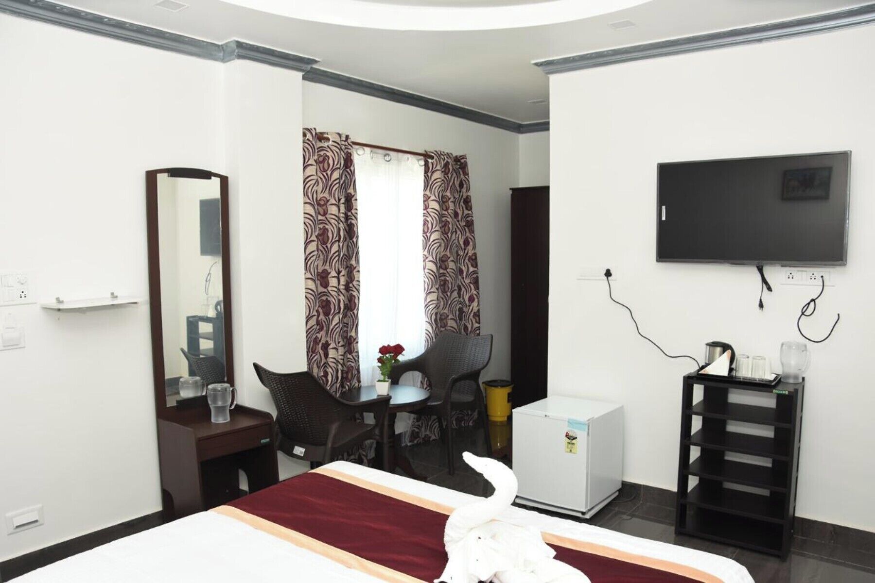 Una habitación de hotel con cama, escritorio, silla, televisor, refrigerador y espejo.