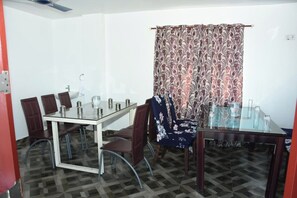 A dining area with a glass-top table, brown chairs, and a patterned curtain. - Sea Shore In (Port Blair)