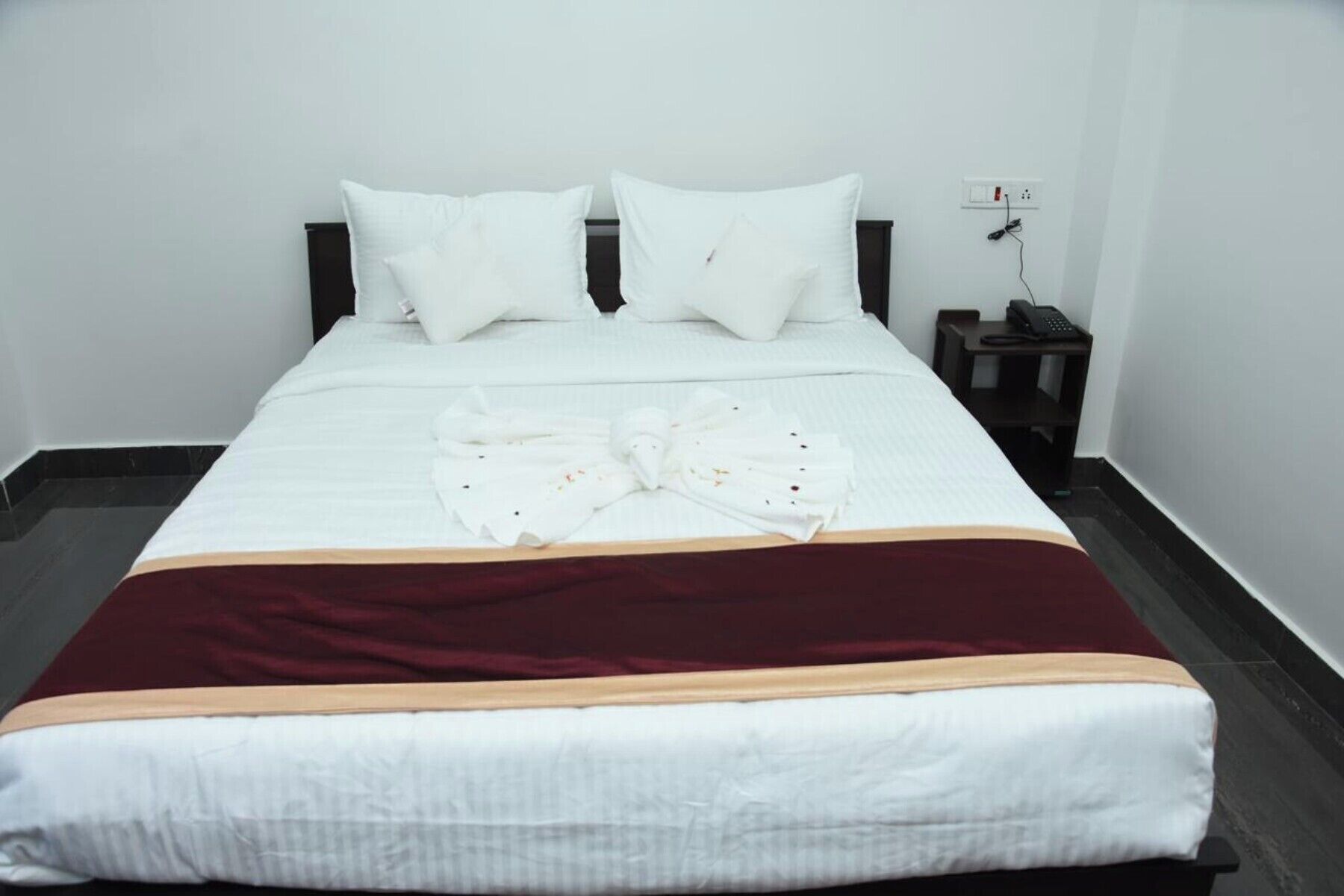 Una cama bien hecha con ropa de cama blanca y una manta color burdeos.