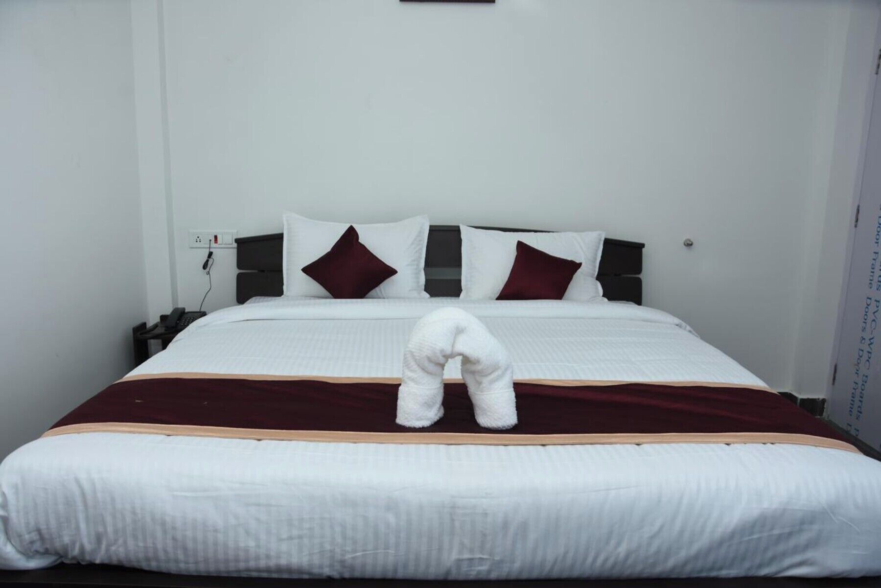 A neatly made bed with white bedding and two dark red pillows.