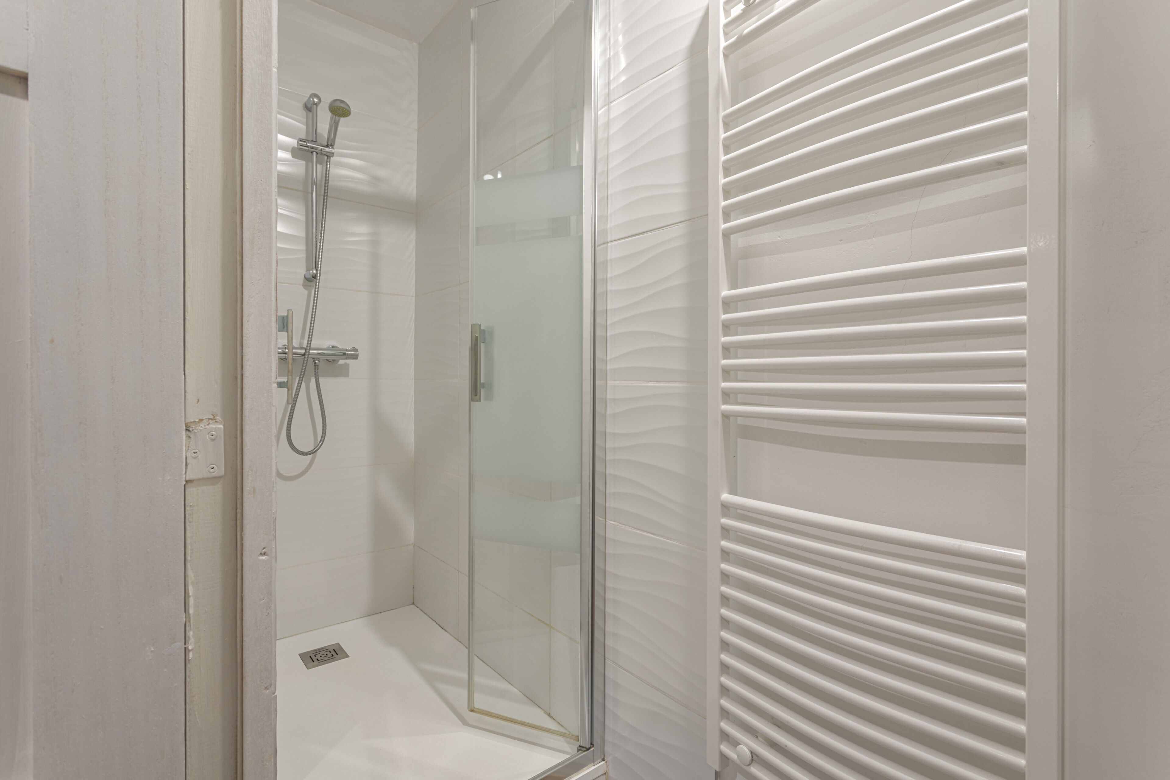 A bathroom with a glass shower enclosure, a white tiled floor, and a white towel rack.