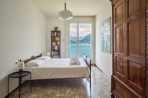 Ein Schlafzimmer mit einem Bett, einem Nachttisch, einem Bücherregal, einem Kleiderschrank und Blick aufs Meer.