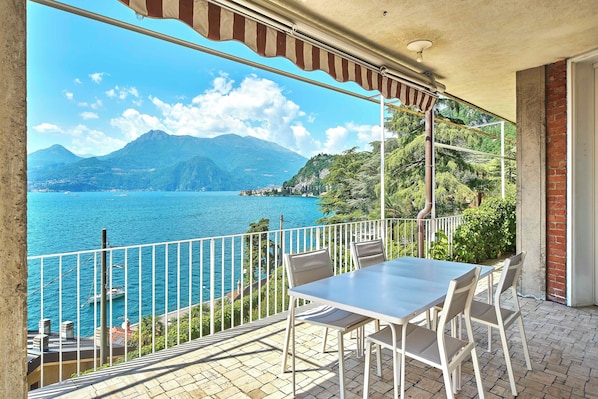 A balcony with a table and chairs, overlooking a body of water and mountains.
