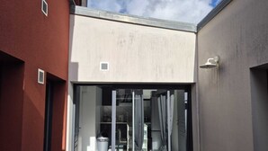 Un bâtiment moderne doté d’une grande porte-fenêtre coulissante qui donne sur un espace intérieur bien éclairé, comprenant un coin salon et une petite table.