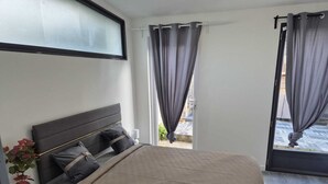 Une chambre à coucher avec un lit, une table de chevet, une plante en pot et une fenêtre avec des rideaux.
