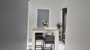 Un couloir étroit avec une porte blanche, une petite table avec deux chaises et une plante en pot.