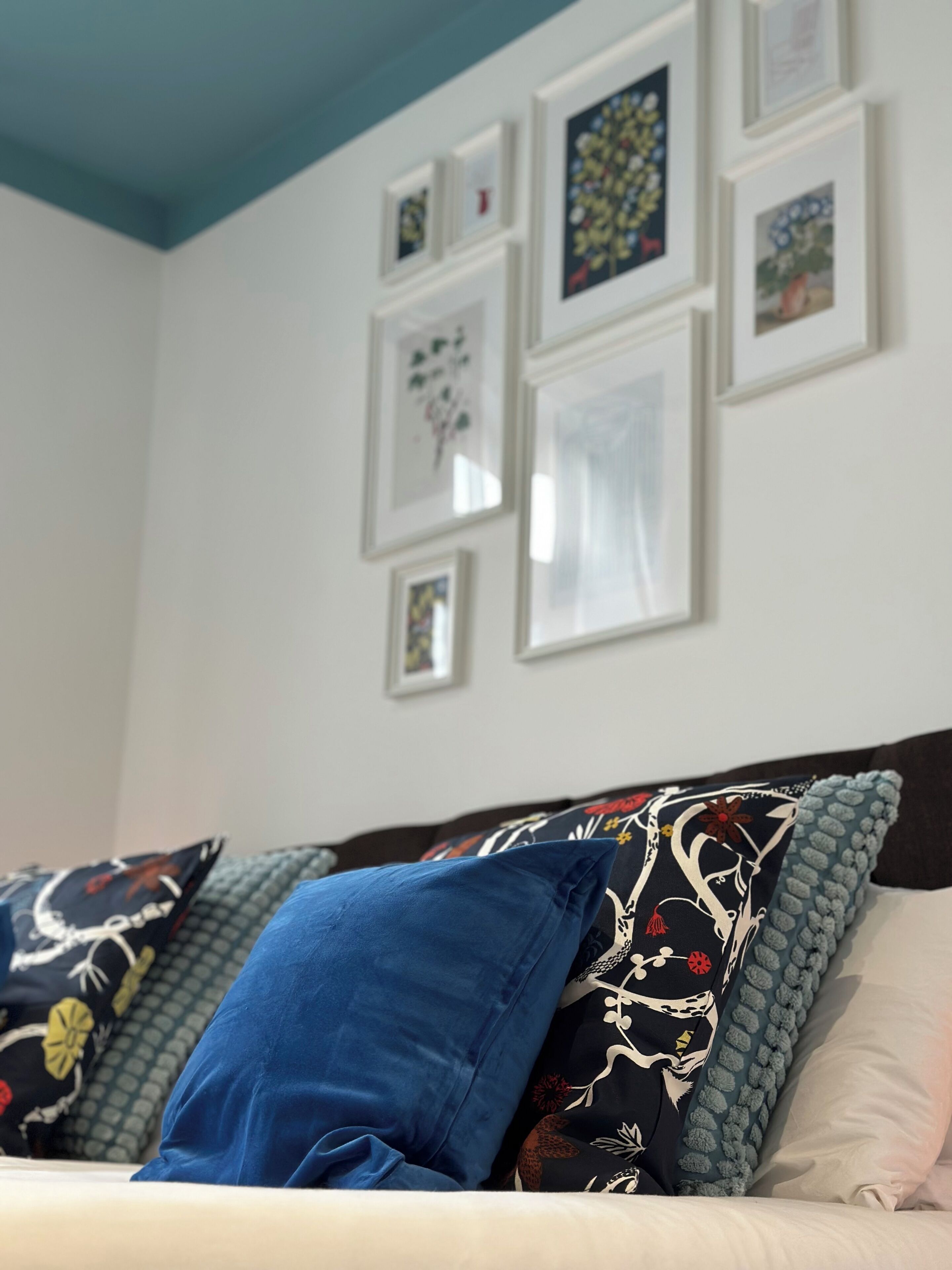 Un dormitorio con cama, almohadas y una pared decorada con cuadros.