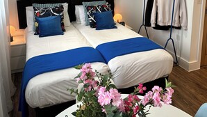 A hotel room with a bed, a bedside table, a wall-mounted air conditioner, a clothing rack, and a wall with framed pictures. - Beautiful studio flat just 3 minutes walk from Tottenham Spur Stadion! (London)