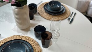 A dining table set with plates, bowls, and cutlery, surrounded by woven placemats and a vase with flowers. - Beautiful studio flat just 3 minutes walk from Tottenham Spur Stadion! (London)