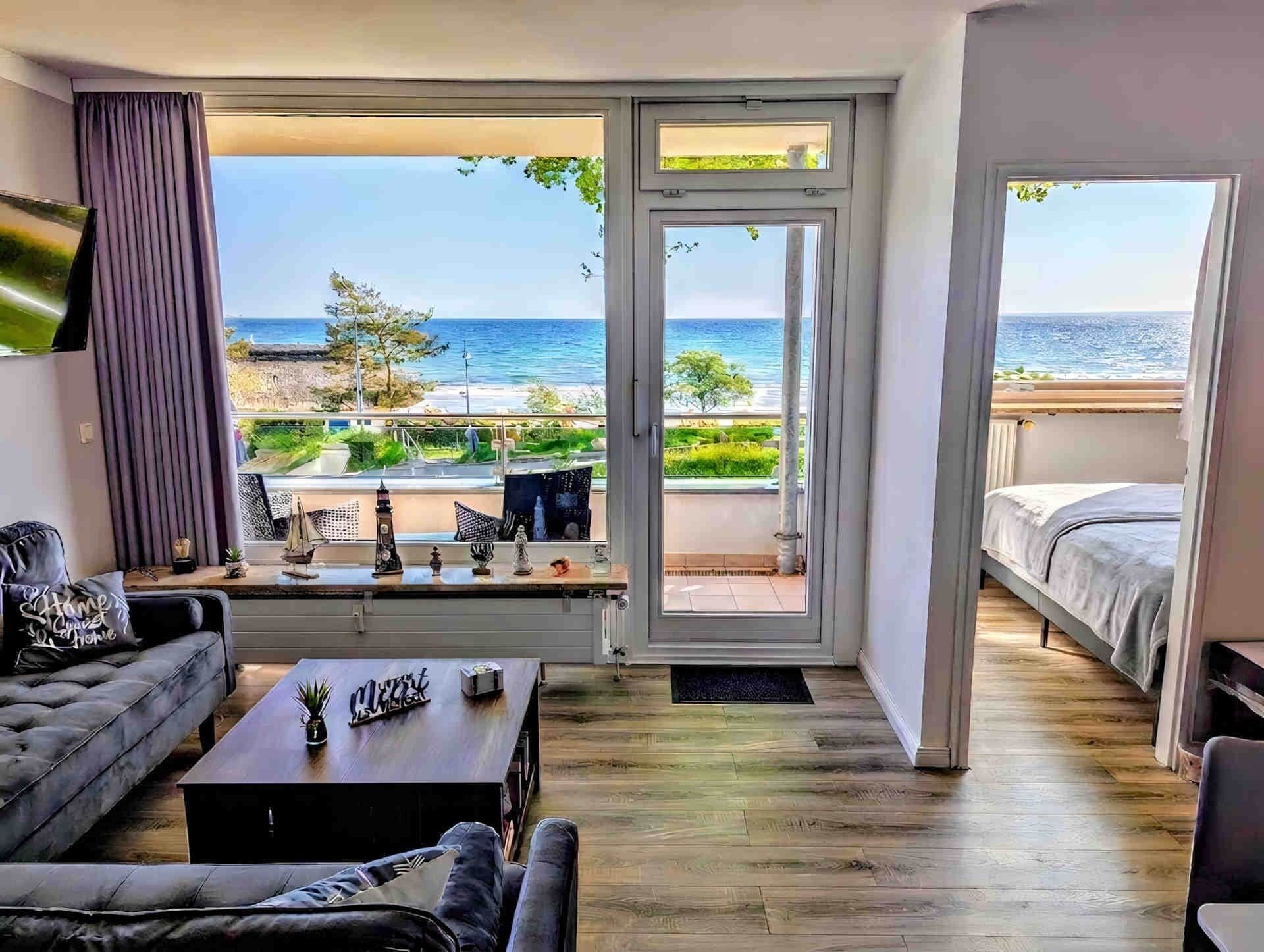 A modern bedroom with a large window offering a view of the sea, a cozy seating area with a sofa and coffee table, and a minimalist design.