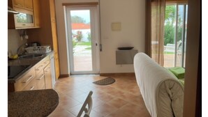 A compact kitchen with a microwave, stove, and sink. A sliding door leads to a balcony with a view of greenery. - Cantinho da Luísa (Coimbrã- Atouguia da Baleia)