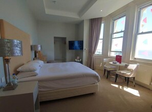 Une chambre d’hôtel avec un grand lit, une télévision, un bureau avec une chaise et une fenêtre avec des rideaux.