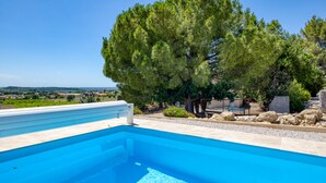 A swimming pool with a clear view of the surrounding landscape, a large tree, and a bench. - Le petit mas du vigné (Saint-Pargoire)