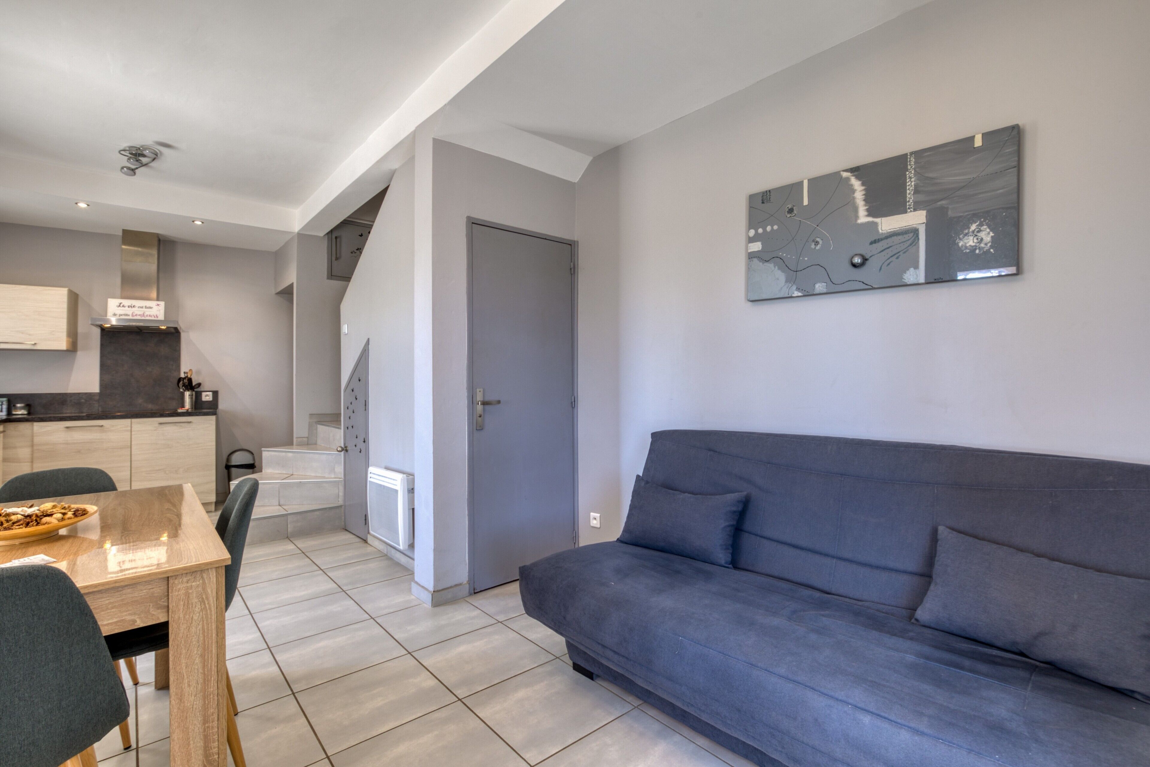 Ein modernes Wohnzimmer mit grauem Sofa, einem Esstisch mit Stühlen, einer Küchenzeile und einer Treppe zu einer weiteren Ebene.