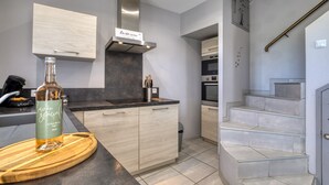 A modern kitchen with a wooden countertop, a stainless steel range hood, and a bottle of wine on a cutting board. - Le petit mas du vigné (Saint-Pargoire)
