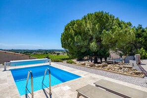 Une piscine avec vue sur la campagne, entourée d’arbres et agrémentée de mobilier d’extérieur.
