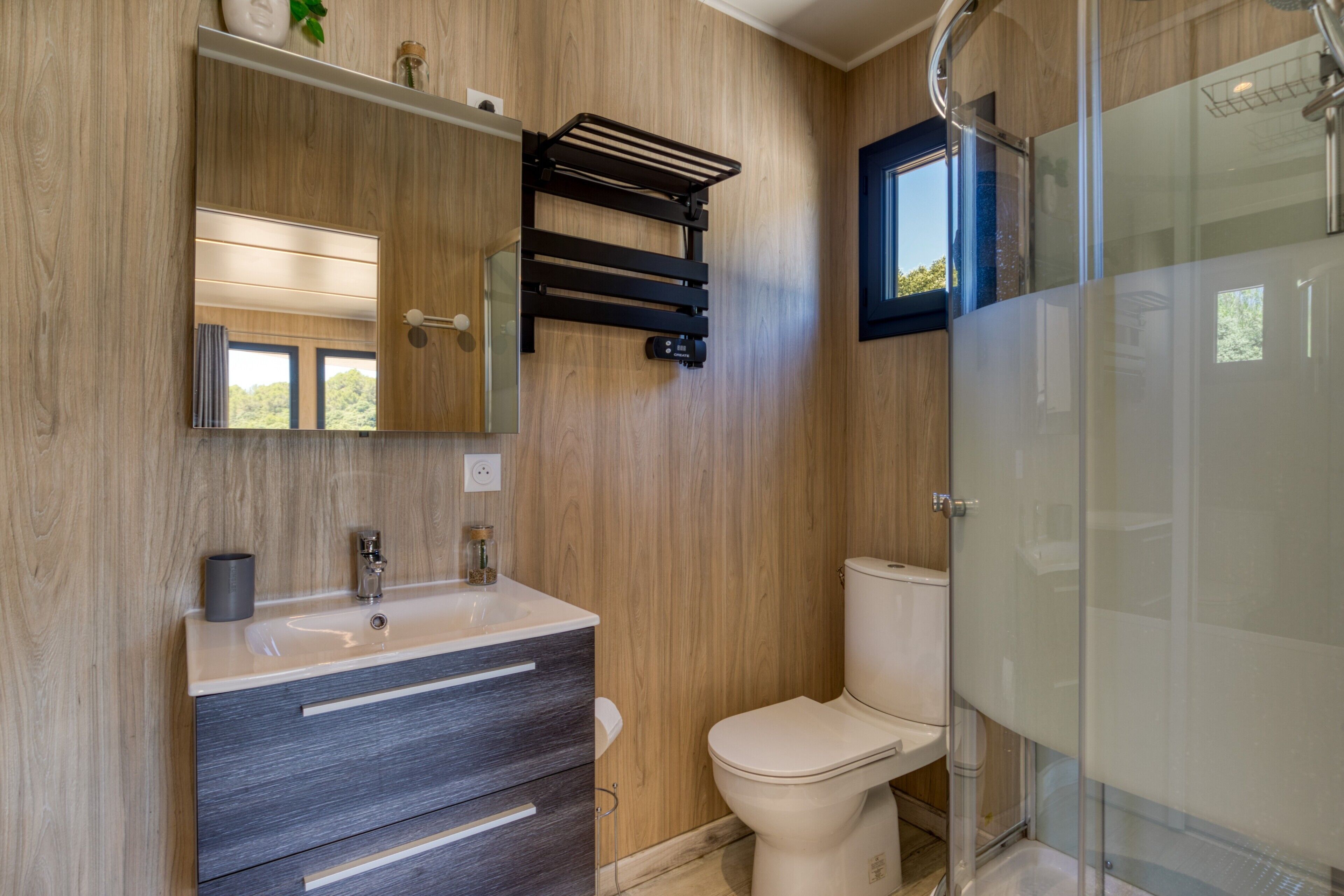 Une salle de bain moderne avec un mur en bois, un lavabo avec un miroir, des toilettes et une douche à parois de verre.
