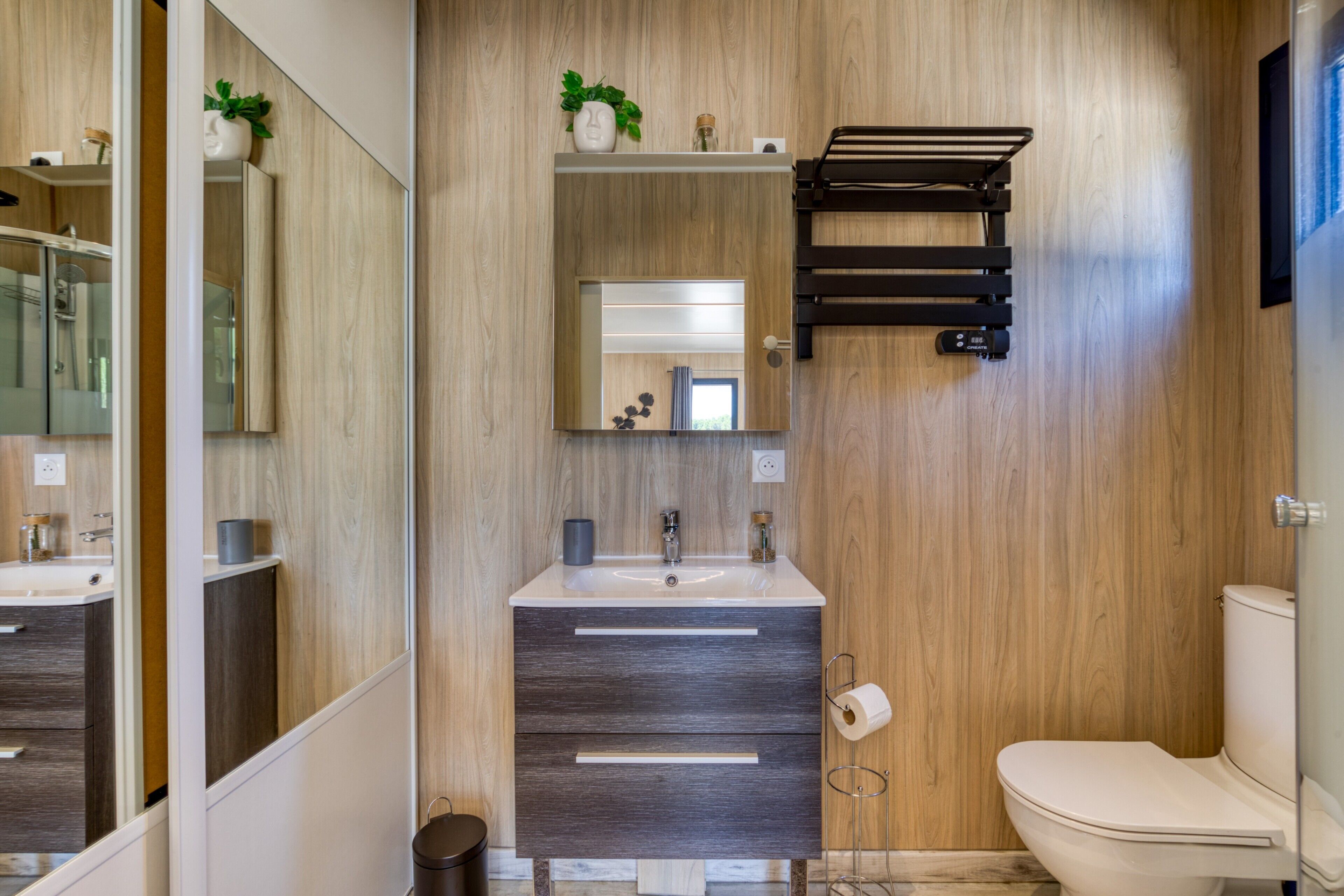 A modern bathroom with a wooden wall, a sink with a mirror, a toilet, and a towel rack.