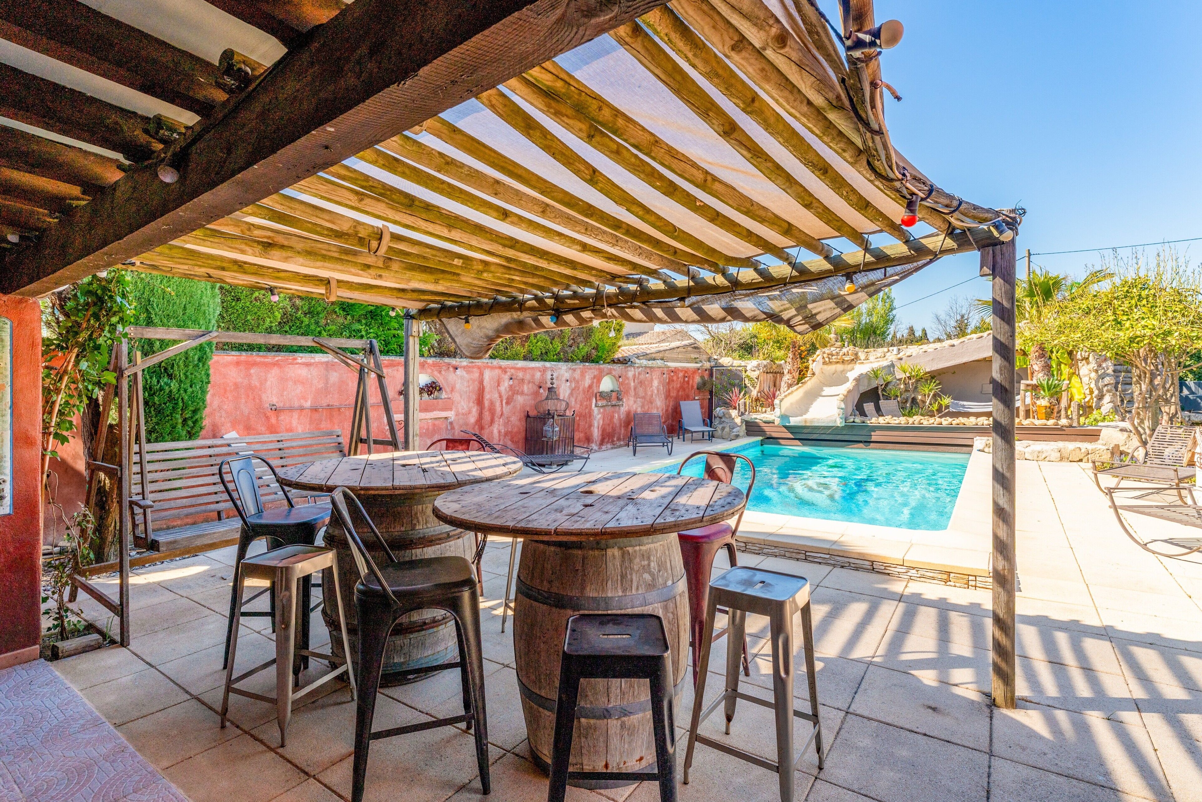 Un espace extérieur abrité, aménagé avec une piscine, des tables et des chaises en bois.