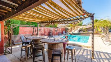 Un espace extérieur abrité, aménagé avec une piscine, des tables et des chaises en bois.
