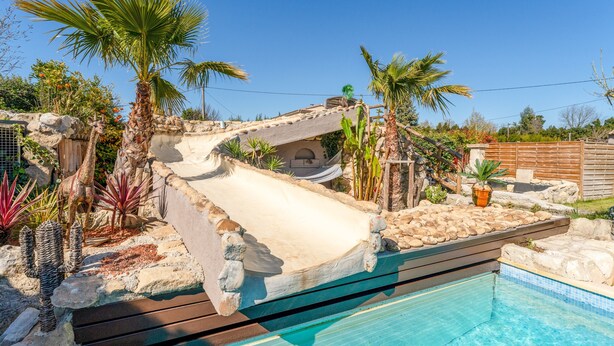 A pool with a slide, palm trees, and a stone wall.