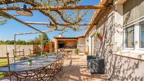 An outdoor patio with a round table and chairs, a pergola with hanging lights, and a stone wall.