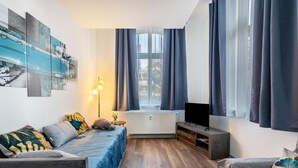 Una sala de estar moderna con un sofá, un televisor, un radiador y una ventana con cortinas.