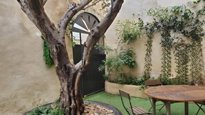 Une cour avec un arbre planté dans un bac, une table en bois et des chaises.