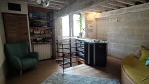Une pièce avec un fauteuil vert, un canapé jaune, une petite table avec une bouilloire, un radiateur et une bibliothèque.