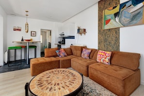 Een moderne woonkamer met een hoekbank, een ronde salontafel en een keuken op de achtergrond.