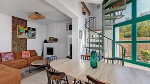 A modern living room with a spiral staircase, a dining area, and a large window with a view of greenery.
