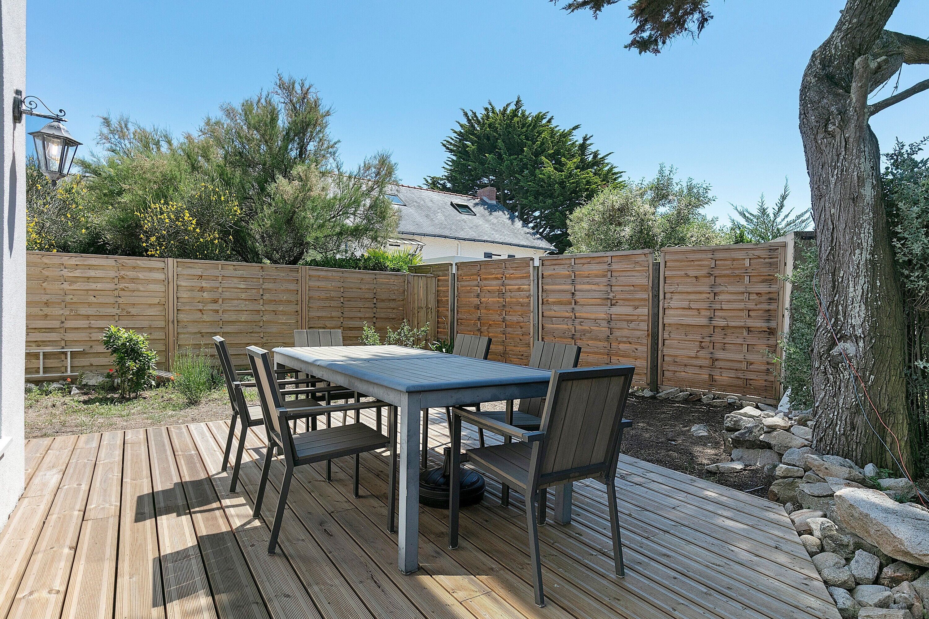 Une terrasse en bois avec une table et des chaises, entourée d’une clôture en bois et d’un arbre.