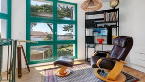 A room with a large window, a rocking chair, a bookshelf, and a small stool.