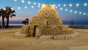 Una estructura de piedra con base circular y parte superior cónica, rodeada por una zona pavimentada con luces de cuerda.