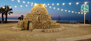 A stone structure with a circular base and a conical top, surrounded by a paved area with string lights. - Private accommodation "Ballatoio233" (Bisceglie)