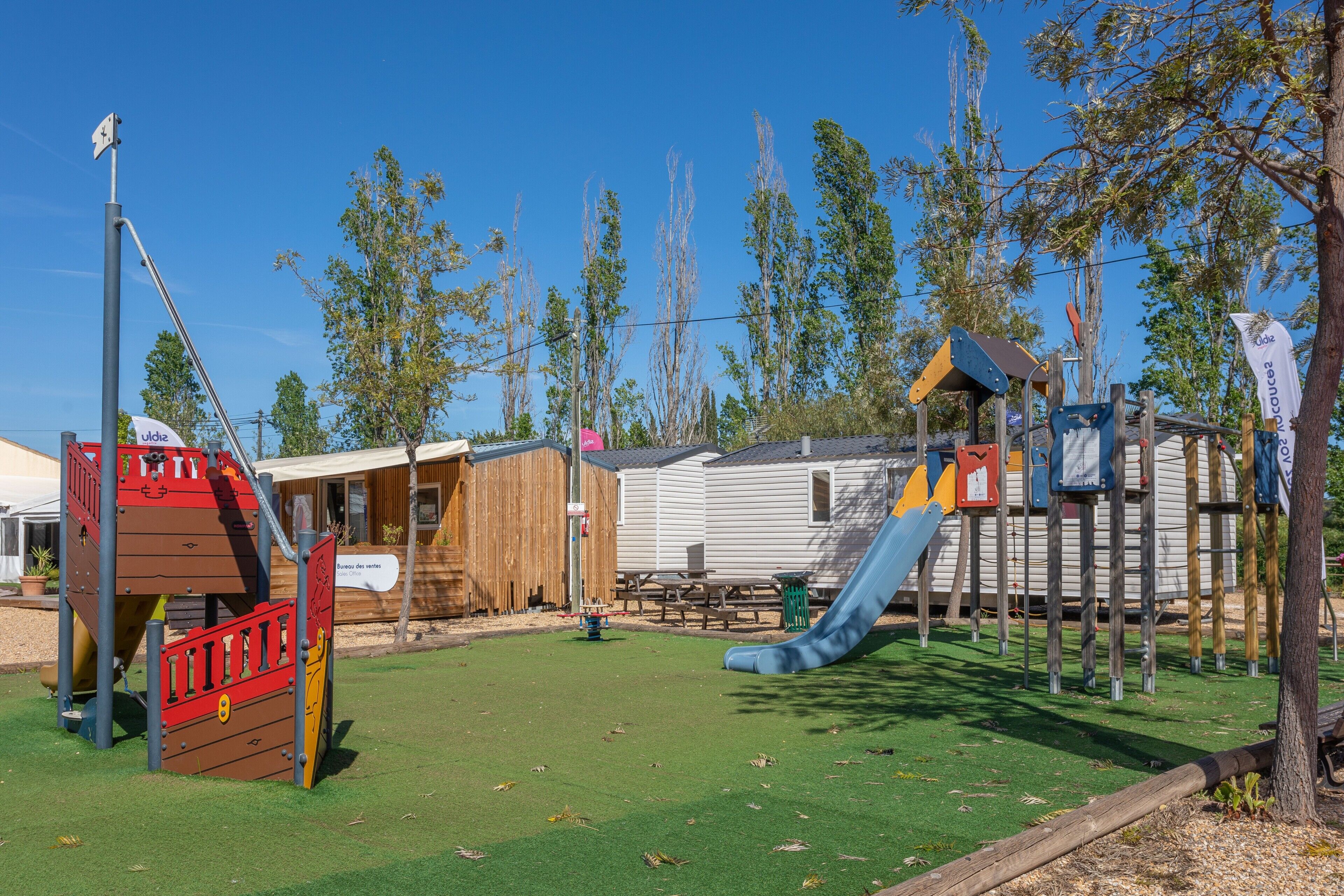 Ein Spielplatz mit Rutsche, Klettergerüsten und Picknicktischen.