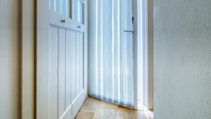Un couloir avec une porte blanche, un rideau à rayures et un sol en pierre.