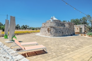Un bâtiment en pierre surmonté d’un dôme, une terrasse dallée avec des chaises longues et un ciel d’un bleu éclatant.