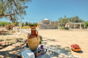 Une cour avec un bâtiment en pierre, un grand vase et des plantes en pot.