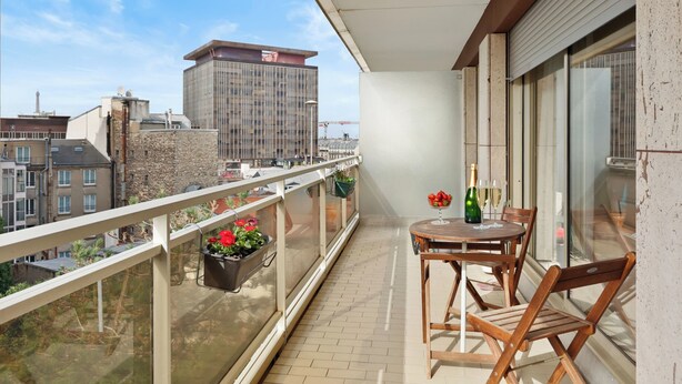 Un balcone con tavolo e sedie, piante in vaso e vista sulla città, con un grattacielo.