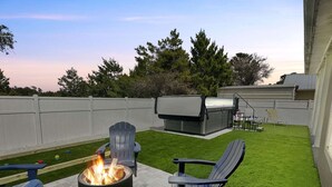 Een achtertuin met een vuurkorf, twee Adirondack stoelen, een barbecue en een gazon.